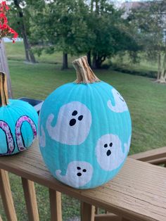 two painted pumpkins sitting on top of a wooden rail