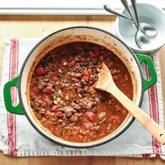 a pot filled with chili and beans on top of a table next to a wooden spoon