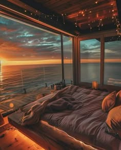 a bed sitting in front of a window on top of a wooden floor next to the ocean