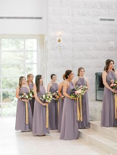 a group of women standing next to each other in front of a window holding bouquets