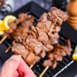 a person is grilling skewers of meat and lemons