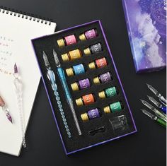 a purple box with pens and markers in it next to a notepad, pencils and an open notebook