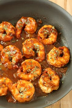 cooked shrimp with sauce and herbs in a skillet on a wooden table, ready to be eaten