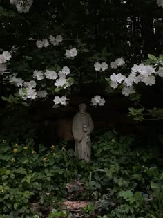 a statue in the middle of some bushes and trees with white flowers growing over it