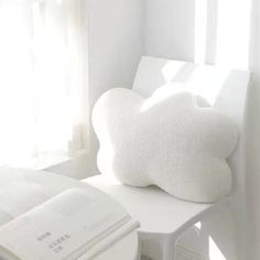 a white chair with a pillow on top of it next to a book and window