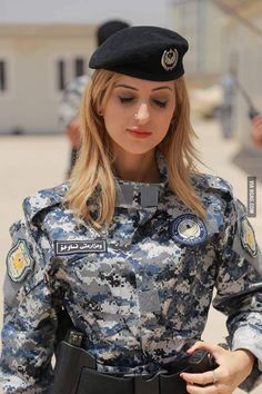 a woman in uniform is holding a cell phone and looking at the camera while standing outside