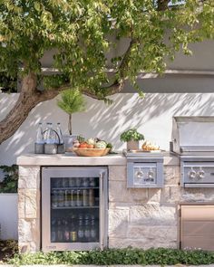 an outdoor kitchen with stainless steel appliances and food on the counter, next to a tree