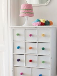 a white dresser with multi colored crochet drawers and a pink lamp on top