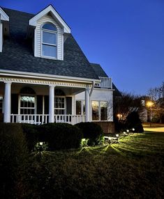 a house that has some lights on in front of it and bushes around the yard