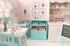 a dollhouse kitchen with pink and blue decor on the walls, white table chairs and shelves filled with cupcakes