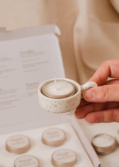 a person is holding a small candle in a white cup with gold dots on it