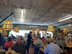 people sitting at tables in a restaurant with yellow lamps hanging from the ceiling above them