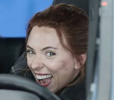 a woman is smiling as she sits in the driver's seat of a car