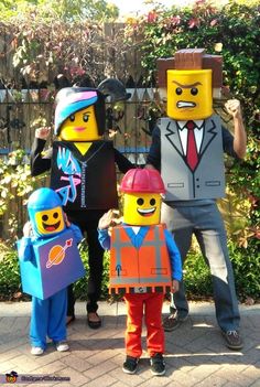 three people in lego costumes standing next to each other on a brick walkway with bushes behind them