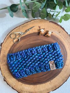 a blue knitted pouch sitting on top of a wooden stump next to some scissors