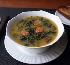 a bowl of soup with carrots and spinach on a plate next to bread