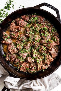 a skillet filled with meat and gravy on top of a white table