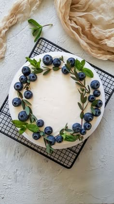 a white cake with blueberries and green leaves on top, sitting on a cooling rack