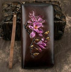 a brown leather wallet with purple flowers painted on the front and side, sitting next to a handbag