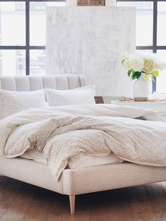 an unmade bed with white linens and flowers in a vase on the end table