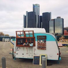 an old camper trailer parked in front of a cityscape with tall buildings