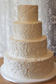 a three tiered white wedding cake sitting on top of a wooden table next to a window