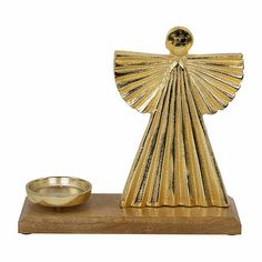 a golden angel figurine next to a gold bowl on a wooden stand with a white background