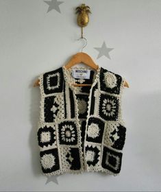 a black and white crocheted vest hanging on a wall next to a pineapple