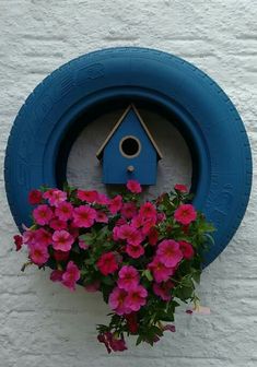 a blue birdhouse hanging on the side of a building with pink flowers in it