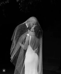 a woman in a wedding dress and veil kissing a man on the forehead with his arm around her