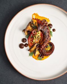 an octopus dish on a white plate topped with olives and other food items,