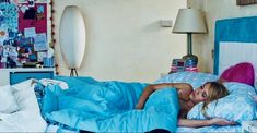 a woman laying on top of a bed under a blue blanket next to a lamp