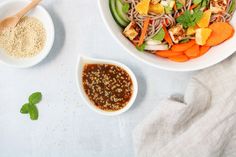 a white bowl filled with food next to another bowl full of vegetables and sauces