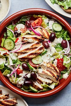 a salad with chicken, cucumbers, tomatoes and olives in a red bowl