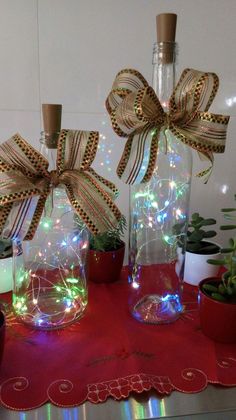 two vases with lights in them sitting on a table next to potted plants