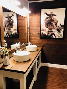 two white sinks sitting on top of a wooden counter next to mirrors and vases