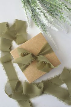 a gift wrapped in brown paper with a green ribbon on it next to some branches