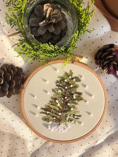 a cross stitch christmas tree on a table with pine cones