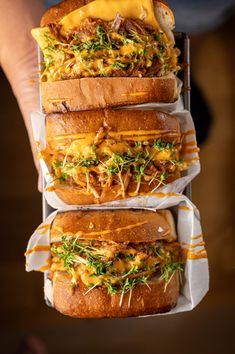 three sandwiches stacked on top of each other with cheese and toppings in paper wrappers