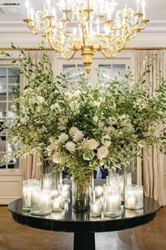 a table with candles and flowers on it in front of a chandelier filled with glass vases