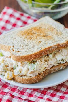 a chicken salad sandwich on a plate with a bowl of lettuce in the background