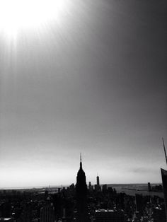 black and white photograph of the empire state building in new york city, with sunbeams