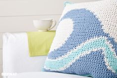 a crocheted pillow sitting on top of a white couch next to a cup