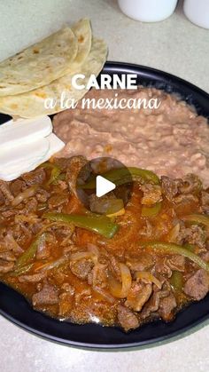 a black plate topped with meat and beans next to tortilla bread on a table