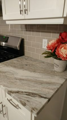 a white kitchen with marble counter tops and flowers in a vase on the stove top