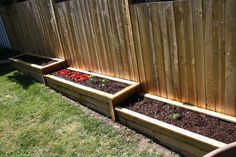 three wooden planters filled with dirt and flowers in the grass near a wood fence