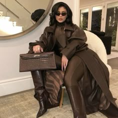 a woman sitting in a chair holding a brown purse and wearing black boots with her legs crossed