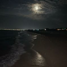 the full moon is shining over the water at night on the beach with waves coming in