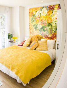 a bed with yellow comforter and pillows in a bedroom next to a painting on the wall