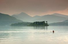 a lone person swimming in the middle of a lake with mountains in the back ground